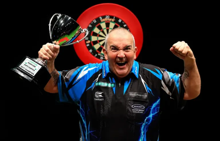 Phil Taylor jubelt mit einer Trophäe vor einer Dartscheibe.