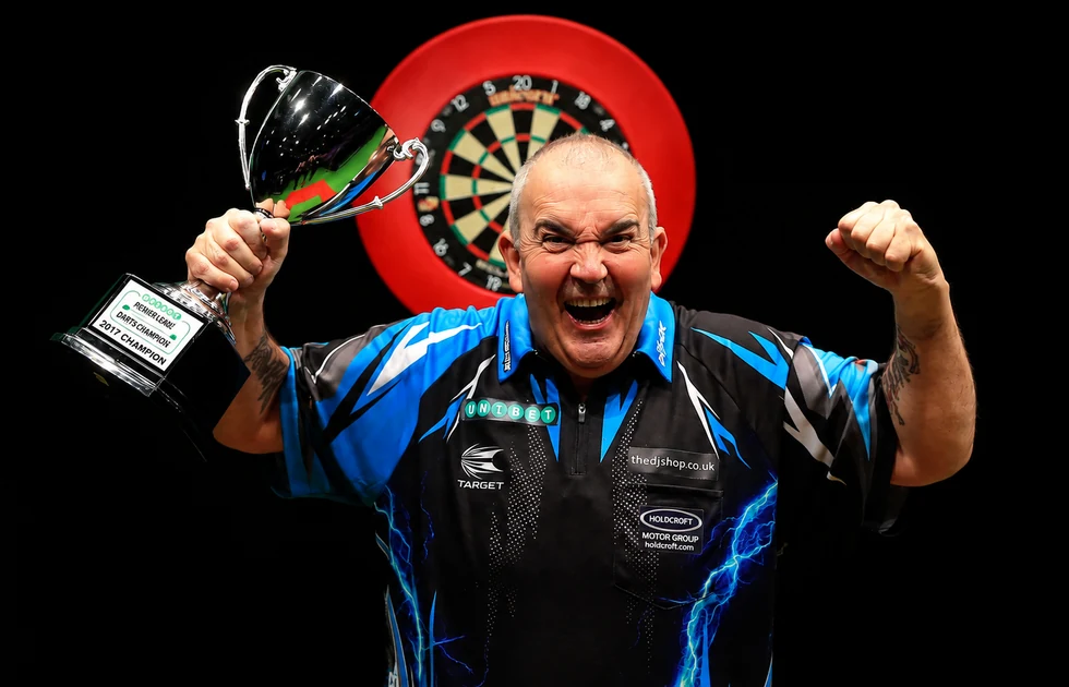 Phil Taylor jubelt mit einer Trophäe vor einer Dartscheibe.