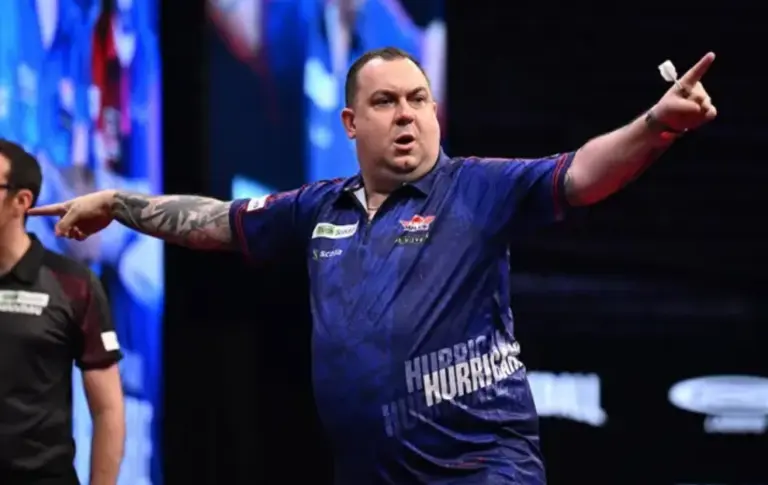 Kim Huybrechts im blauen Dartstrikot mit ausgestreckten Armen auf der Bühne bei einem PDC-Dartturnier.