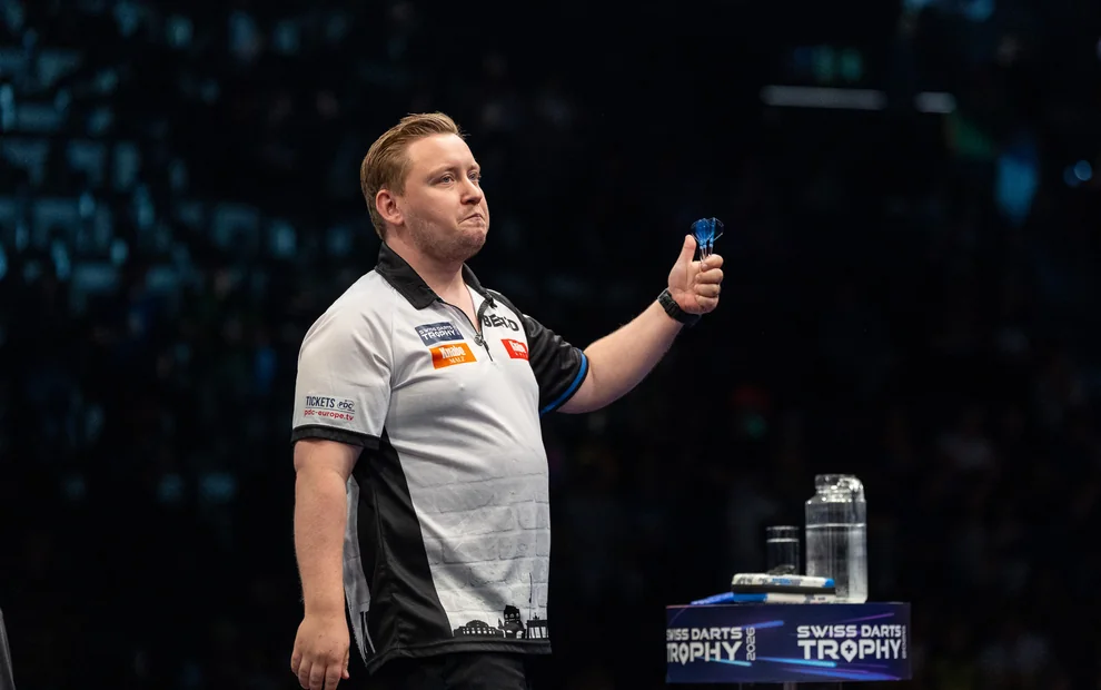 Martin Schindler hält bei der Swiss Darts Trophy 2026 drei blaue Dartpfeile in der Hand.