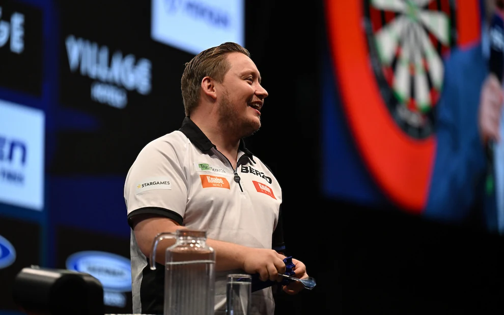 Martin Schindler lächelt auf der Bühne der European Championship 2026 in Dortmund, mit einer Dartscheibe im Hintergrund.