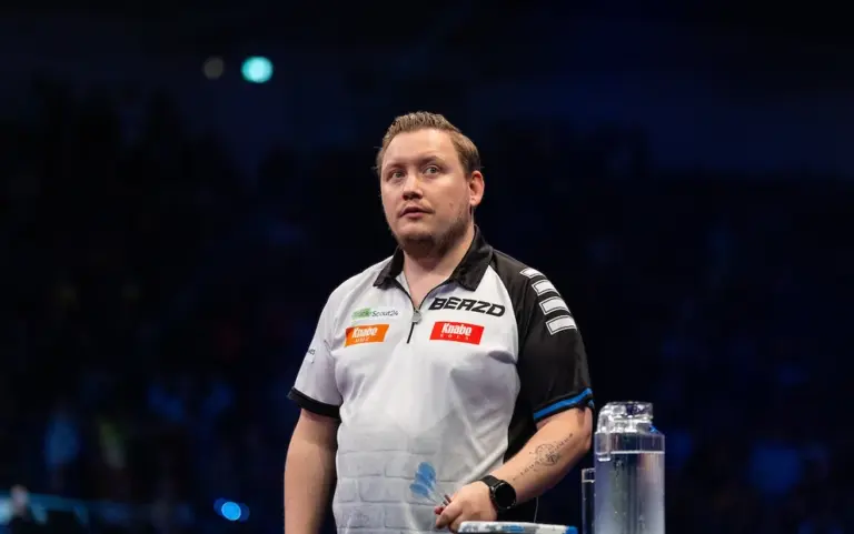 Martin Schindler steht bei der European Darts Championship 2026 auf der Bühne und hält mehrere blaue Darts in der Hand.
